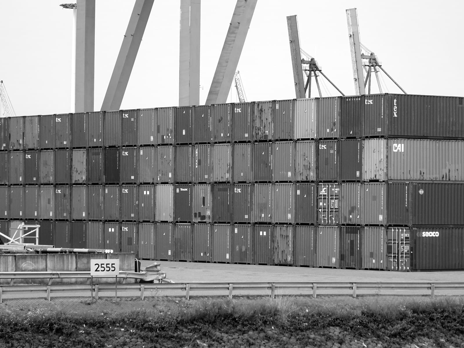 Stacked shipping containers at the Port of Rotterdam, gantry cranes behind them